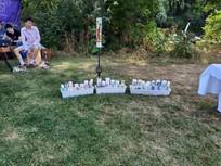Lange Reihe von Taufkerzen am Boden auf der Wiese, dahinter Kerzenständer mit großer Kerze. Im Hintergrund zwei Jugendliche.
