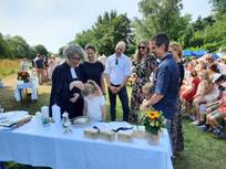 Pfarrerin Schlarb tauft ein Mädchen am Altar auf der Wiese am Neckar in Kirchheim. Die Familie steht um die beiden herum, im Hintergrund sitzt die Gemeinde auf Stühlen.