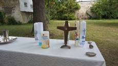 Altar mit weißem Tischtuch im Garten. Auf dem Altar Taufkelch, Tablett, Tauffkerzen und Kreuz.
