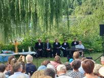 Fünf Pfarrerinnen und Pfarrer im Talar beimTauffest auf der Neckarwiese, daneben der Altar mit Kreuz, davor die Gemeinde, der Kantor sitzt am Keyboard.