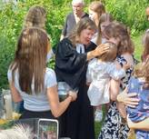 Pfarrerin Kurlberg legt auf der Neckarwiese ihre Hand zum Segen auf den Kopf eines Babys. Baby auf dem Arm der Mutter, umstehend Mädchen.